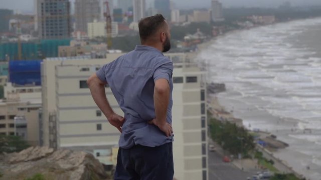 Young man standing on cliff admire view of the city, ocean, slow motion