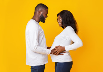 Smiling husband holding his wife belly over yellow background