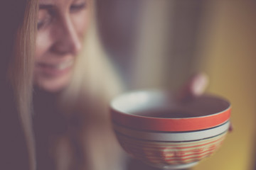 Large orange bowl with tea in hands of a smiling young woman, soft selective focus on the mug.