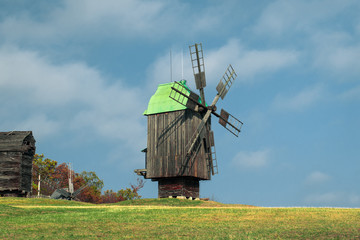 Old wooden windmill on the hill. Wooden mill with a green roof. Windmill on an abandoned farm