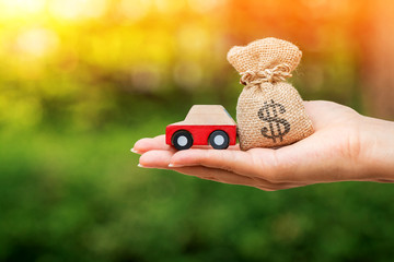 Women hand holding a car model and money bag on bokeh in the public park, Loan for buy a new car or...