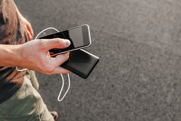 man hands holding black smartphone charging battery from external power bank