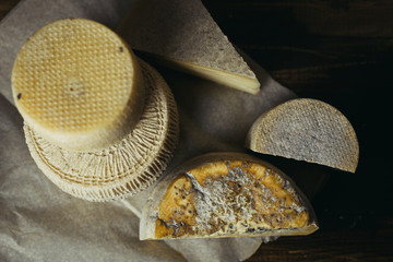 Different homemade cheeses on a dark wooden background. Pieces and cheese heads of Gorgonzola, Asiago, Maasdam, Gauda, Paramezan and Edam. Goat and cow cheese on baking paper. Handwork, Flat lay