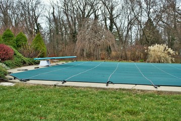 backyard swimming pool with diving board and pool slide tarped up and closed down for winter