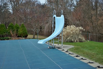 backyard swimming pool with diving board and pool slide tarped up and closed down for winter