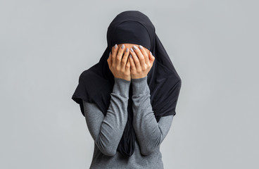 Muslim woman in black hijab covering face with hands
