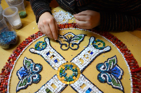 Female hands with tweezers spread a picture of smalt in a mosaic workshop. Capacities with smalt. Making a red circle with a pattern inside. Selective focus.