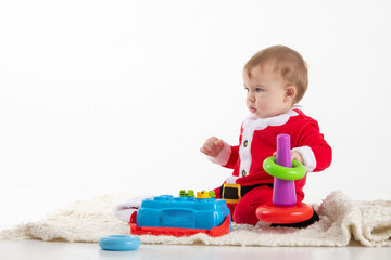 baby dressed as Santa Claus sitting on the floor playing with toys