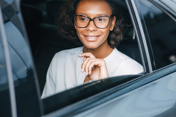 Smiling businesswoman sitting on a backseat of the taxi and looking away. Young entrepreneur in a...