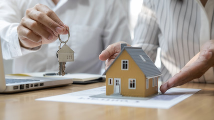 Real estate agent holding a key and asking costumer for contract to buy, get insurance or loan real estate or property.