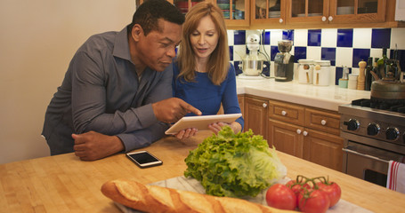 Mature couple standing in kitchen looking at recipe on tablet computer