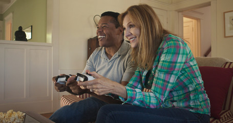 Happy older couple playing video games together on living room couch