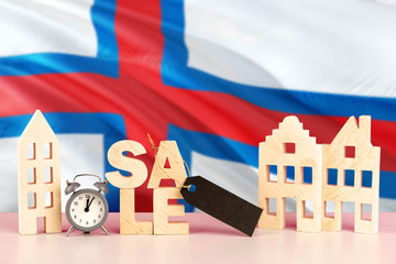 Faroe Islands real estate sale concept. Wooden house model with discount tag on national flag background. Copy space for text.