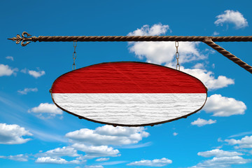 Monaco flag on a signboard. Oval signboard colors Monaco flag hanging on a metal forged structure. Template on a background of blue sky with clouds.