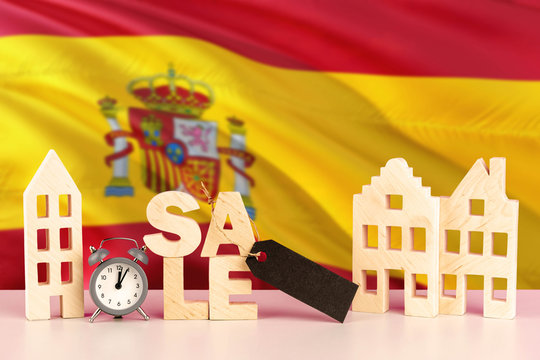 Spain real estate sale concept. Wooden house model with discount tag on national flag background. Copy space for text.