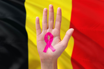 Belgium awareness concept. Close-up awareness ribbon painted on palm on national flag background. October Pink day and world cancer day.
