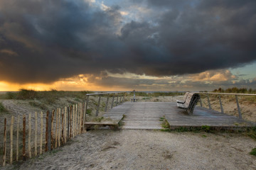 Two benches on a plateau on a dune top under thick rain clouds