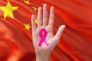 China awareness concept. Close-up awareness ribbon painted on palm on national flag background. October Pink day and world cancer day.