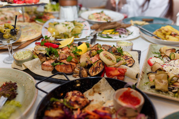 festive table setting in restaurant for special event with grilled vegetables, meat, olives and sauce