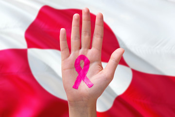 Greenland awareness concept. Close-up awareness ribbon painted on palm on national flag background. October Pink day and world cancer day.
