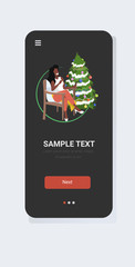african american woman sitting on armchair near christmas tree xmas new year winter holidays celebration concept smartphone screen online mobile app full length vector illustration