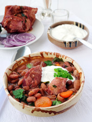 Pinto bean soup with smoked ham hock in bowl with sour cream and red onions on the table, vertical