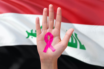 Iraq awareness concept. Close-up awareness ribbon painted on palm on national flag background. October Pink day and world cancer day.