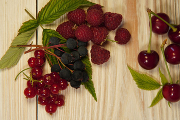 red currant, raspberry, cherry, leaves, cereals on a light wood background.