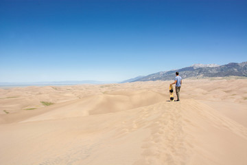 Fototapeta na wymiar young man with sand board on sand dune in great sand dunes national park colorado