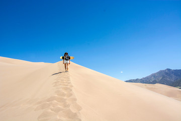 woman with sand board walking on edge of a sand dune in the great sand dunes national park, colorado united states of america