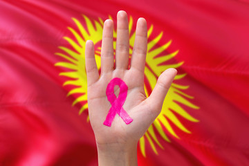 Kyrgyzstan awareness concept. Close-up awareness ribbon painted on palm on national flag background. October Pink day and world cancer day.