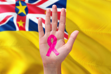 Niue awareness concept. Close-up awareness ribbon painted on palm on national flag background. October Pink day and world cancer day.
