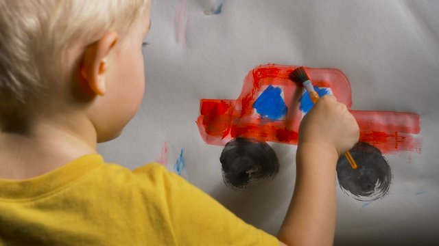 Little boy (preschooler) is painting a red toy truck with watercolor paint. Indoor kids activities, daycare, classroom. Early education concept, child creativity and art