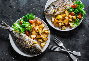 Delicious family lunch table - dorado fish baked with potatoes, lemon and sage on dark background, top view