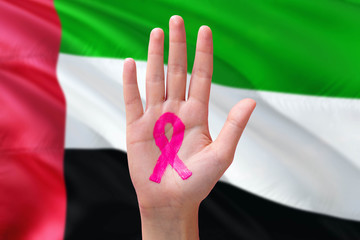 United Arab Emirates awareness concept. Close-up awareness ribbon painted on palm on national flag background. October Pink day and world cancer day.