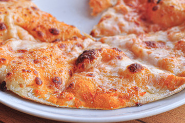  A close-up of sliced ​​golden-orange cheese pizza on a white plate on a brown table in natural daylight, without one slice with spreading melted cheese of different varieties and colors