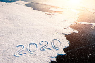 Inscription of new year 2020 on the snow surface on ice. Winter holiday background
