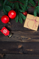 Gift and burning candles on a dark wooden table with fir branches close-up top view