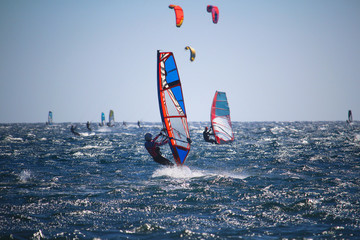 Windsurfers and kitesurfers on choppy sea, in backlight