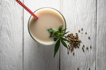 Hemp milk is poured into a glass. On the surface is a cannabis leaf. Nearby marijuana seeds