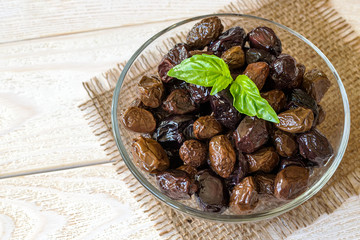 Sun-dried or cured olives in a glass bowl on a white rustic wooden table. Healhy eating and vegetarian food. Ingredient for tapenade, sandwich or salad.