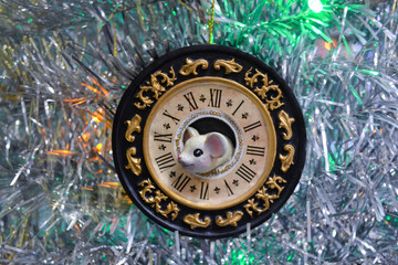 White mouse-a symbol of the Chinese new year, looks out of the old clock on the background of bright silver tinsel with colorful. Concept of new year holidays, midnight