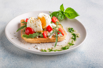 French breakfast concept. Poached egg on toasted bread with cherry tomatoes, cheese and herbs on a boiled background