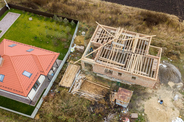 Top down aerial view of two private houses, one under construction with wooden roofing frame and...
