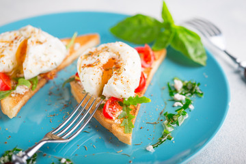 Two poached eggs on toasted toast with cherry tomatoes, cheese and herbs on a large blue plate