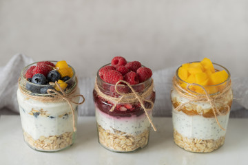 Three glass jars with delicious yogurt pudding with сhia seeds, oats, berries and jam on a marble board. The concept of healthy eating, diet.