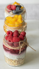 Three glass jars with delicious yogurt pudding with сhia seeds, oats, berries and jam on a marble board. The concept of healthy eating, diet.