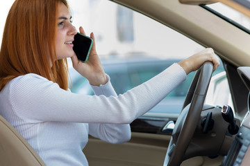 Happy redhead girl talking on her mobile phone behind the wheel driving a car.