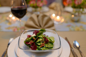 First course salad in home dinning room table set for a dinner party with napkin and red wine