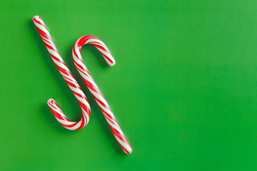 Two christmas red and white candy canes on a textured green paper background.